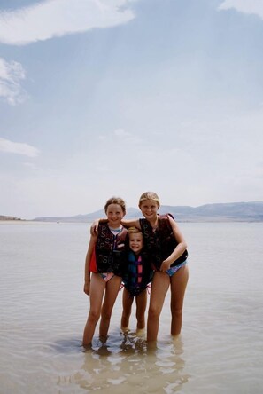 Four people standing in shallow water with a clear sky and distant mountains in the background.