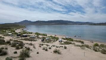 A beach with camping trailers and a boat, surrounded by sand dunes and mountains.