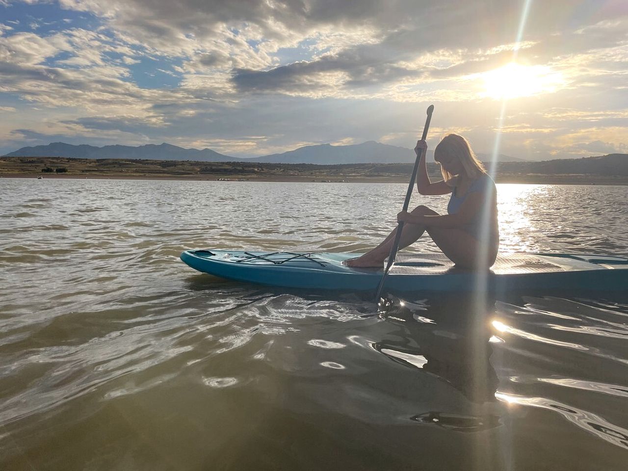 A person paddleboarding on a calm body of water with a mountainous landscape in the background.