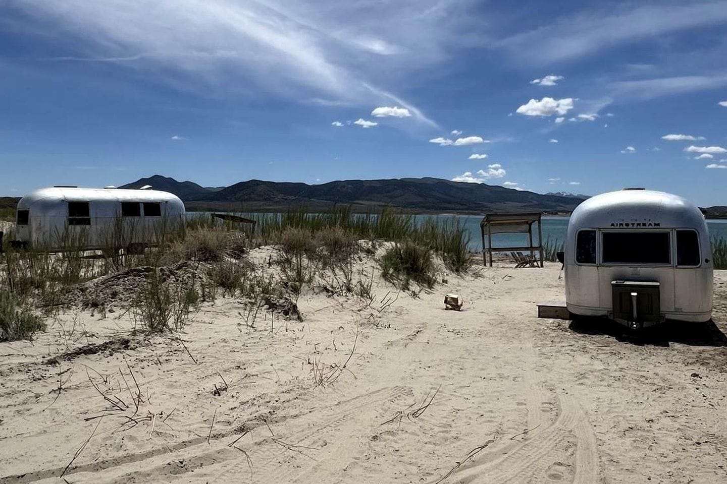 Two trailers on a sandy beach with a lake and mountains in the background.