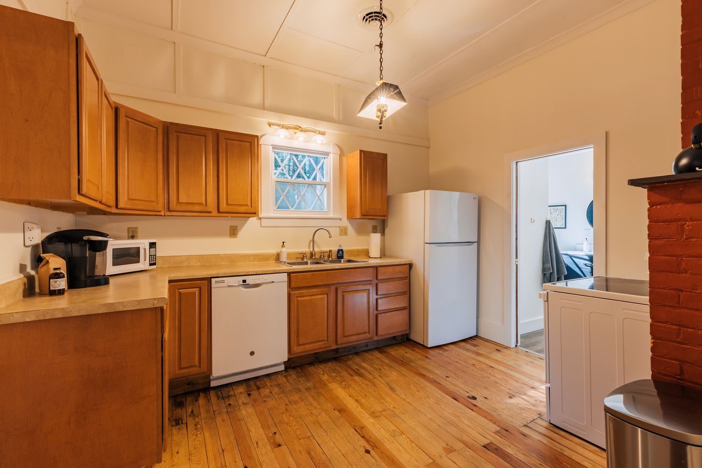 Una cocina con armarios de madera, microondas, lavavajillas, refrigerador y ventana con vistas.