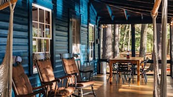 A wooden porch with rocking chairs and a table, surrounded by trees.