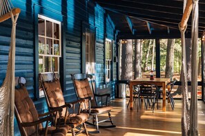 A wooden porch with rocking chairs and a table, surrounded by trees. - Spacious Waterfront Cabin with Private Dock Near Lake George & Saratoga Springs, Corinth, NY (Corinto)