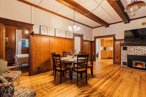 A dining area with a wooden table and chairs, a fireplace, and a kitchen in the background. - Spacious Waterfront Cabin with Private Dock Near Lake George & Saratoga Springs, Corinth, NY (Corinto)