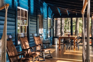 A wooden porch with rocking chairs and a table, surrounded by trees.