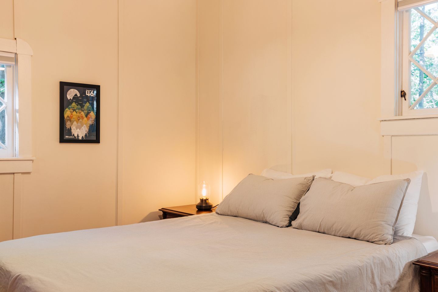 Un dormitorio con una cama, almohadas, una mesita de noche, una lámpara y un cuadro en la pared.