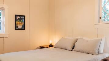 Un dormitorio con una cama, almohadas, una mesita de noche, una lámpara y un cuadro en la pared.