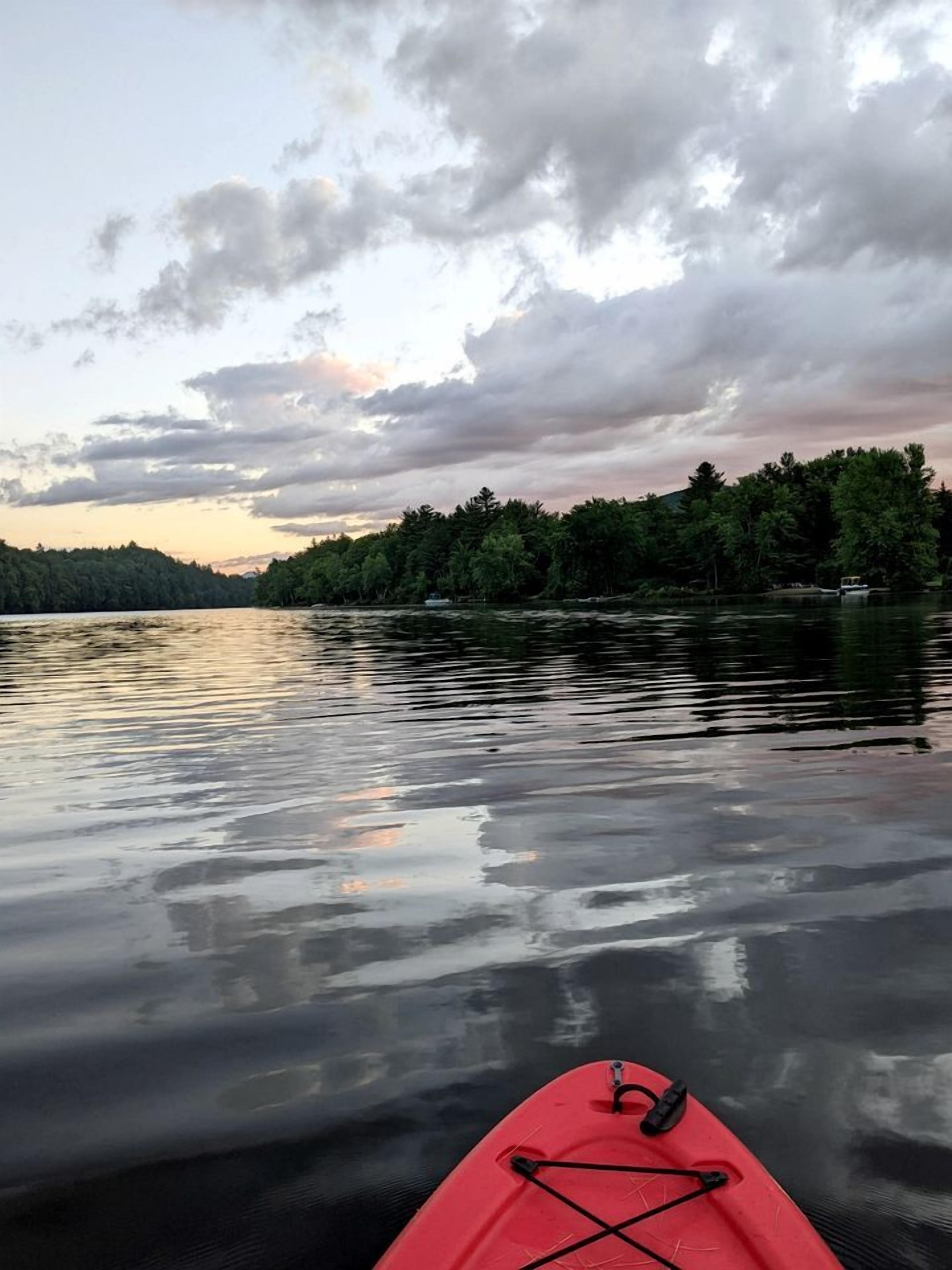 Un lago tranquilo con un kayak rojo en primer plano y una orilla boscosa al fondo.