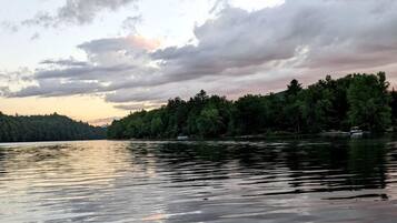 Un lago tranquilo con un kayak rojo en primer plano y una orilla boscosa al fondo.