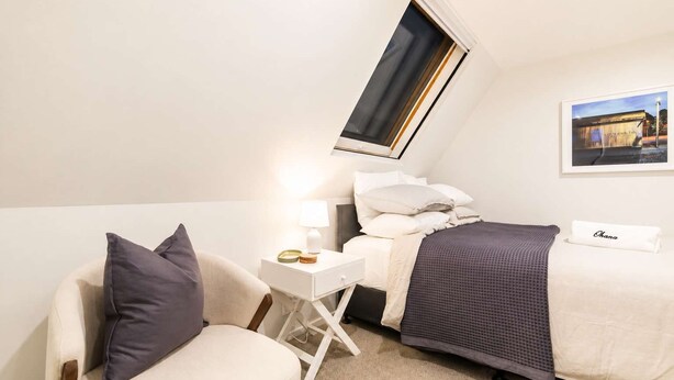 Ein Hotelzimmer mit einem Bett, einem Nachttisch mit Lampe, einem Sessel und einem Fenster.