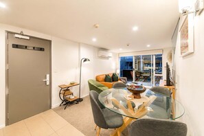 A modern living room with a glass dining table, a sofa, and a floor lamp. - Serene CBD Stay | 2BR | Balcony + Laundry (Christchurch)