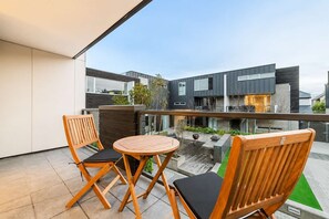 Ein Balkon mit zwei Holzstühlen und einem kleinen runden Tisch, mit Blick auf ein modernes Gebäude mit großen Fenstern.