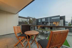 Ein moderner Balkon im Freien mit zwei Holzstühlen und einem kleinen runden Tisch, mit Blick auf eine zeitgemäße Stadtlandschaft.