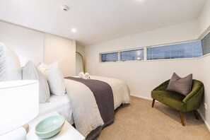 A bedroom with a bed, bedside table, lamp, and a green armchair. - Serene CBD Stay | 2BR | Balcony + Laundry (Christchurch)