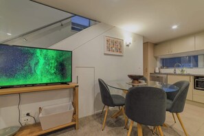 Eine moderne Küche mit Essbereich, einem großen Flachbildfernseher und einer Treppe, die in eine obere Ebene führt.