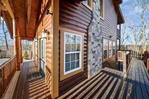 A log cabin with a wooden deck, a stone wall, and a window with blinds. - Glorious Wooden Cabin with Swimming Pool in Pigeon Forge, Tennessee (Pigeon Forge)