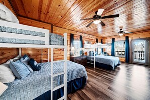 Ein schlicht eingerichtetes Schlafzimmer im Blockhausstil mit Etagenbetten, Holzwänden und Deckenventilator.