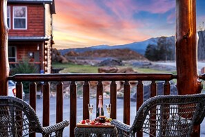 Ein Holzbalkon mit Korbstühlen, einem Tisch mit Flasche und Gläsern sowie einem schönen Bergblick.