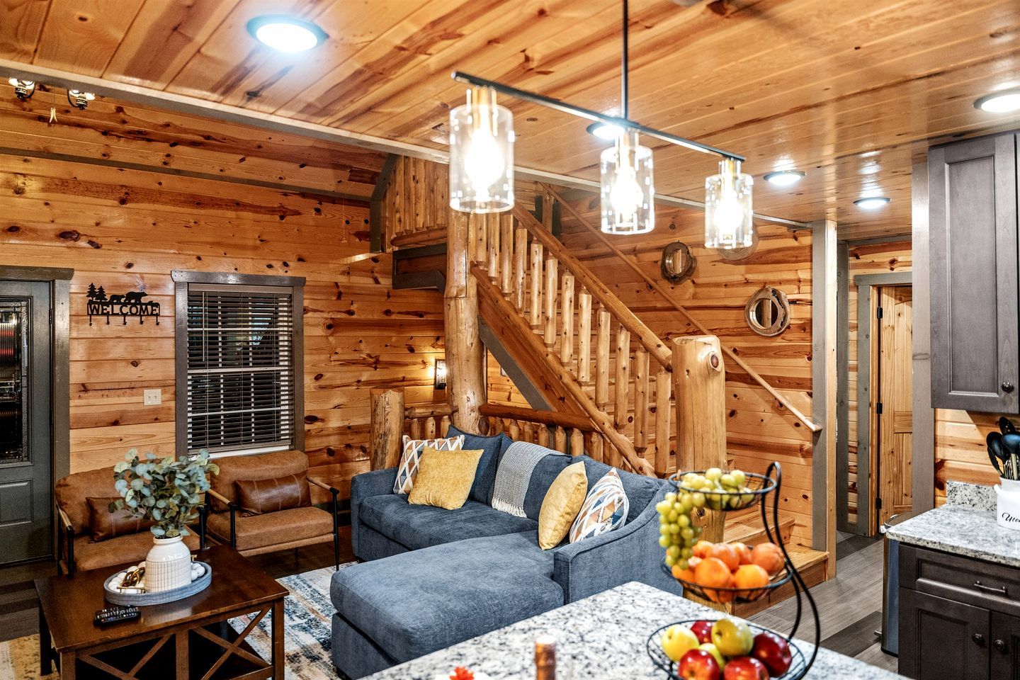 A log cabin interior with a wooden staircase, a sofa, a coffee table, and a fruit bowl.
