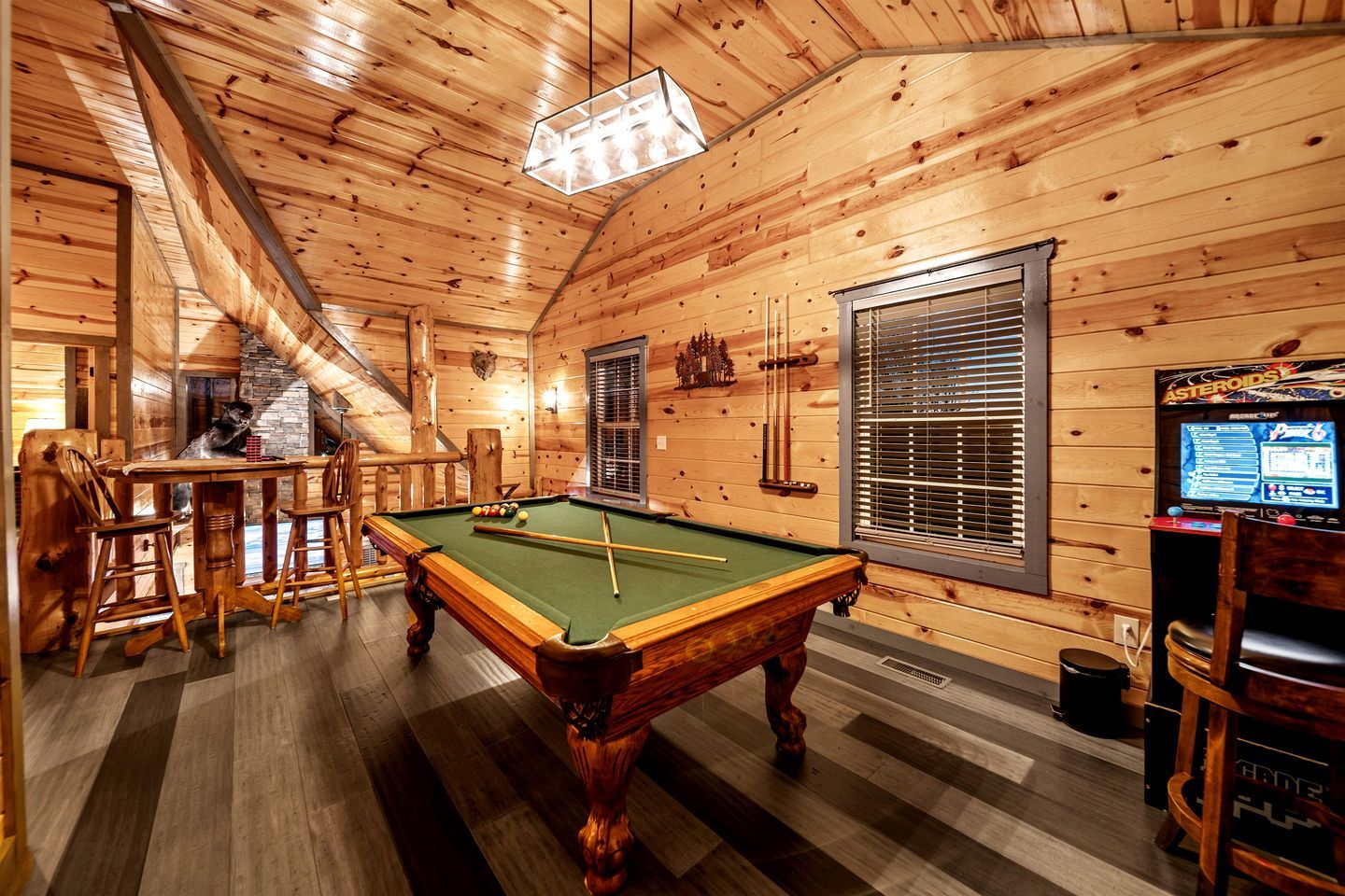 Un intérieur en bois comprenant une table de billard, des tabourets de bar, un porte-taquets et une queue de billard.