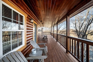 Eine Holzterrasse mit Adirondack-Stühlen und einem Tisch, mit Blick auf eine natürliche Landschaft.