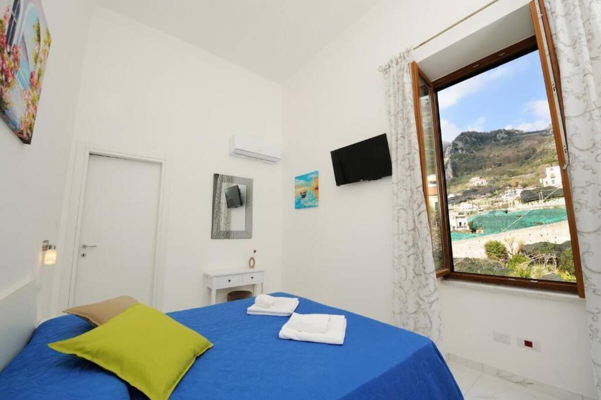 Un dormitorio con cama, televisor, ventana con vistas y puerta.