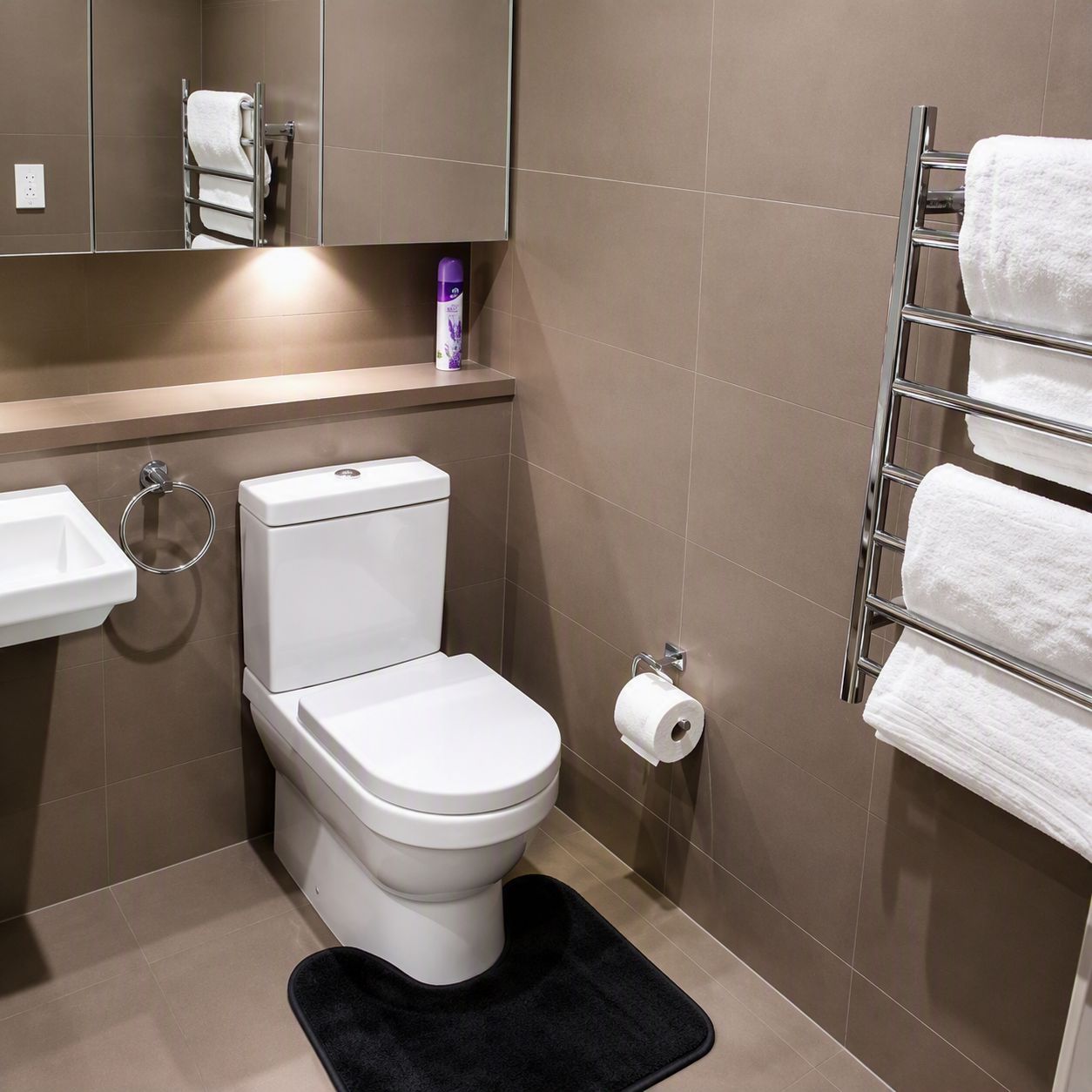 A modern bathroom with a toilet, sink, towel rack, and a black bath mat.