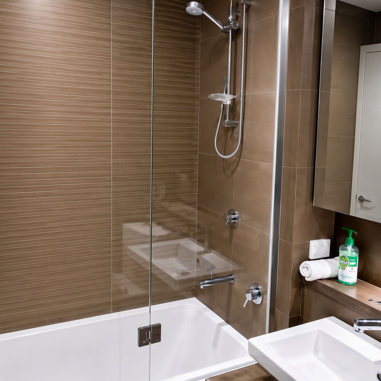A modern bathroom with a glass-enclosed shower, a white bathtub, and a sink with a mirror above it.