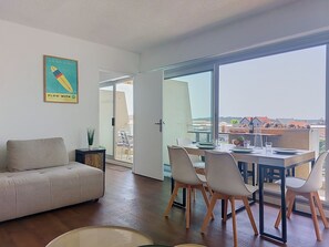Un salon moderne comprenant un canapé, une table à manger, des chaises et une grande porte-fenêtre coulissante donnant sur un balcon.