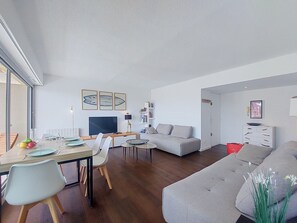A modern living room with a sofa, a dining table with chairs, a TV, and a bookshelf. - Apartment Casino by Interhome (Lacanau)