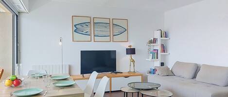 Un salon moderne comprenant un coin repas, un canapé, un téléviseur et des œuvres d’art encadrées accrochées au mur.