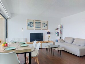 Ein modernes Wohnzimmer mit Essbereich, einer Couch, einem Fernseher und gerahmten Kunstwerken an der Wand.