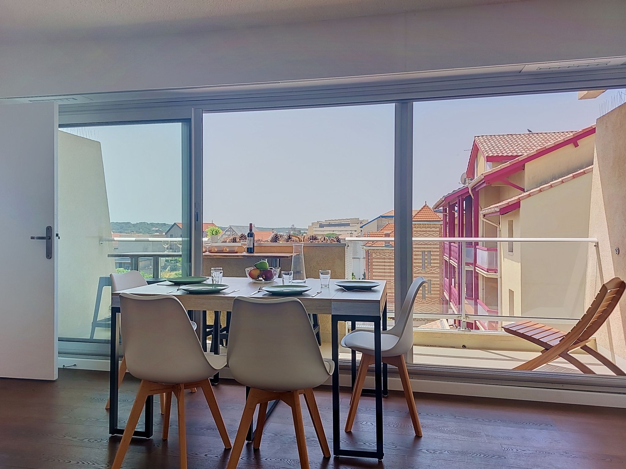 A dining area with a table set for four, large windows, and a view of buildings and a balcony.