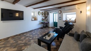 Uma sala de estar com uma televisão de tela grande, uma poltrona de massagem, um sofá, uma mesa de centro e um piso estampado.