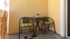 Zwei Korbstühle mit grünen Kissen, ein kleiner runder Tisch mit einem rosafarbenen Topf und eine strukturierte gelbe Wand.