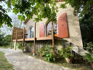 Ein Haus mit einer Holzterrasse, einem Fenster mit Rollläden und Blumentöpfen.