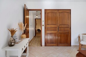 A hallway with a white console table, a wooden double door, and a wicker chair.