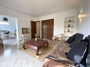 Ein Wohnzimmer mit einer Couch, einem Couchtisch, einem Essbereich mit einem Stuhl, einer Holztür und einem an der Wand befestigten Regal.