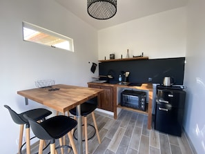 Eine kleine Küche mit Holztisch, schwarzen Stühlen, einer Mikrowelle, einem Kühlschrank und einer schwarzen Arbeitsplatte.