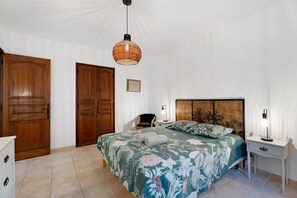 Un dormitorio con una cama grande, una mesita de noche, una lámpara, un armario de madera y una lámpara colgante.