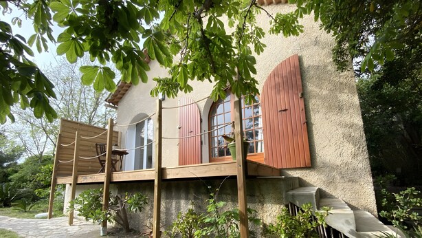 A house with a wooden deck, potted plants, and a stone pathway.