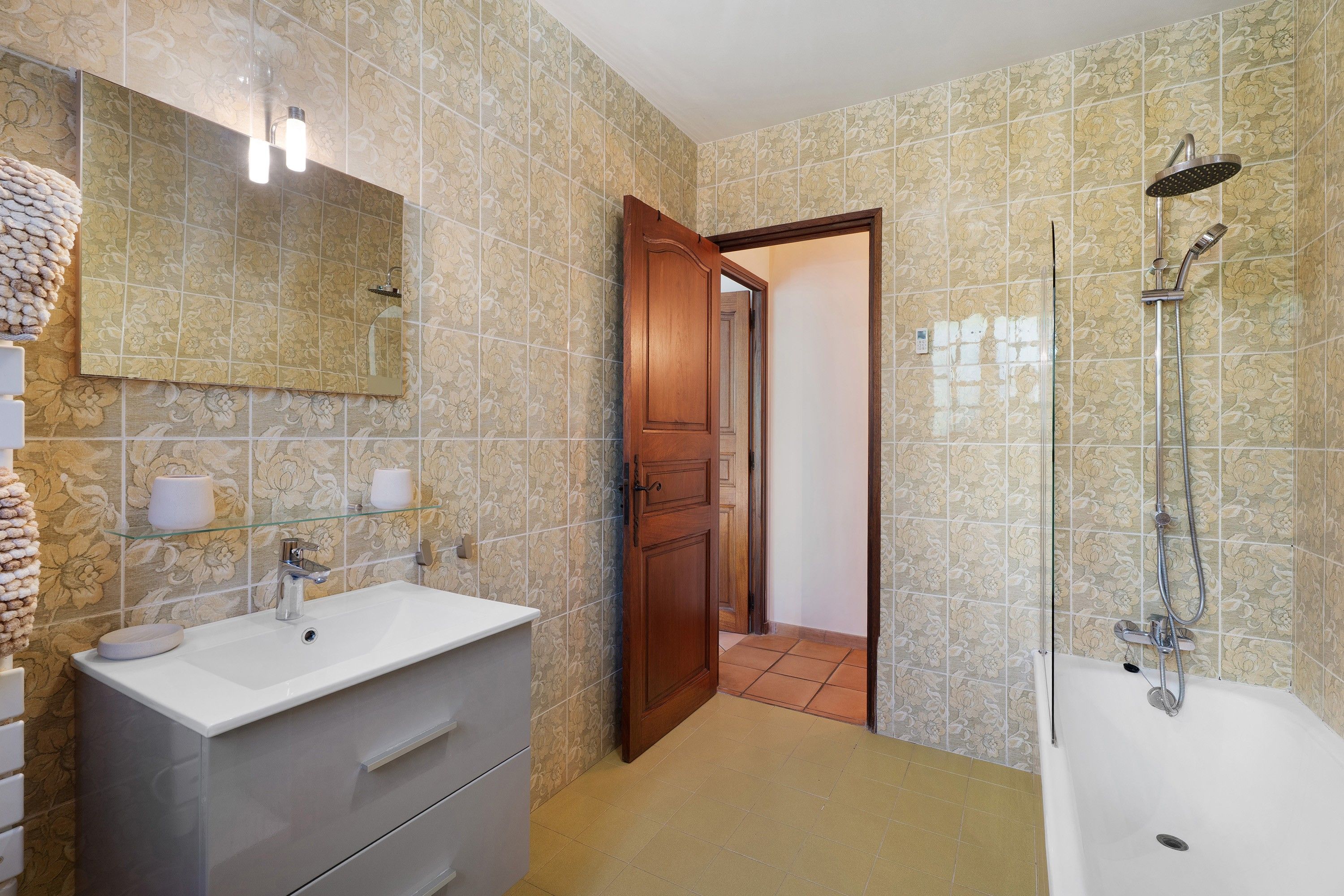 A bathroom with a sink, mirror, shower, and a wooden door leading to another room.
