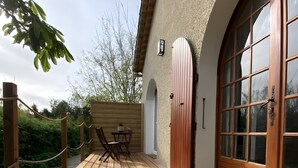 Un terrazzo in legno con tavolo e sedie, una recinzione di legno e un edificio con ampie finestre e un portone.