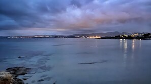 A coastal scene with calm waters, a distant shoreline with buildings, and a mountain range in the background.