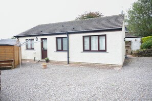 A single-story house with a gravel driveway, a wooden door, and a window with a curtain. - Peaceful Lake District home, near Ennerdale Water (Kirkland)