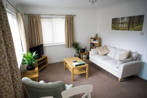 A living room with a sofa, a coffee table, a TV on a stand, a bookshelf, and a window with curtains. - Peaceful Lake District home, near Ennerdale Water (Kirkland)