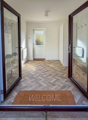 A hallway with a herringbone floor pattern leading to a door with frosted glass panels. A welcome mat is placed at the entrance. - Peaceful Lake District home, near Ennerdale Water (Kirkland)