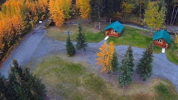 Eine Lodge mit drei Hütten, umgeben von Wald und Bergen.