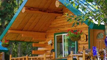 A wooden cabin with a sloped roof, a porch with wooden railings, and a hanging flower basket.