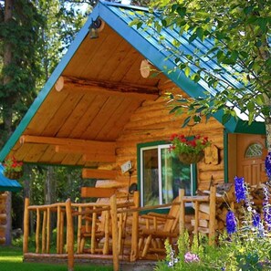 Una baita di legno con tetto spiovente, un portico con ringhiere in legno e un cesto di fiori pensile.